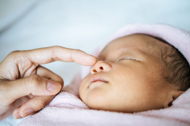 The mother's hand touches the nose of the newborn baby